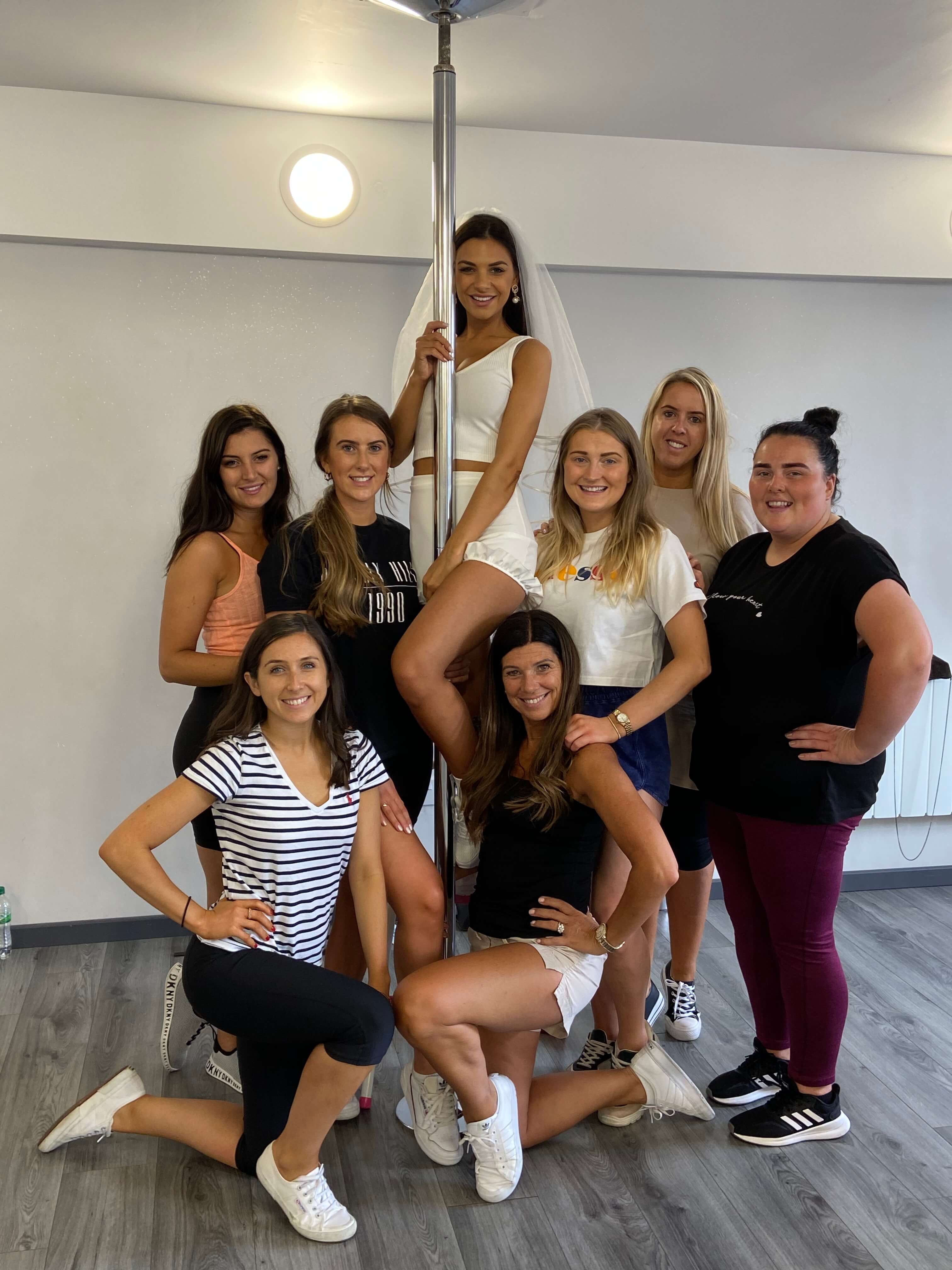 Pole dancing hen party class Leeds - group of women learning pole fitness moves in professional studio